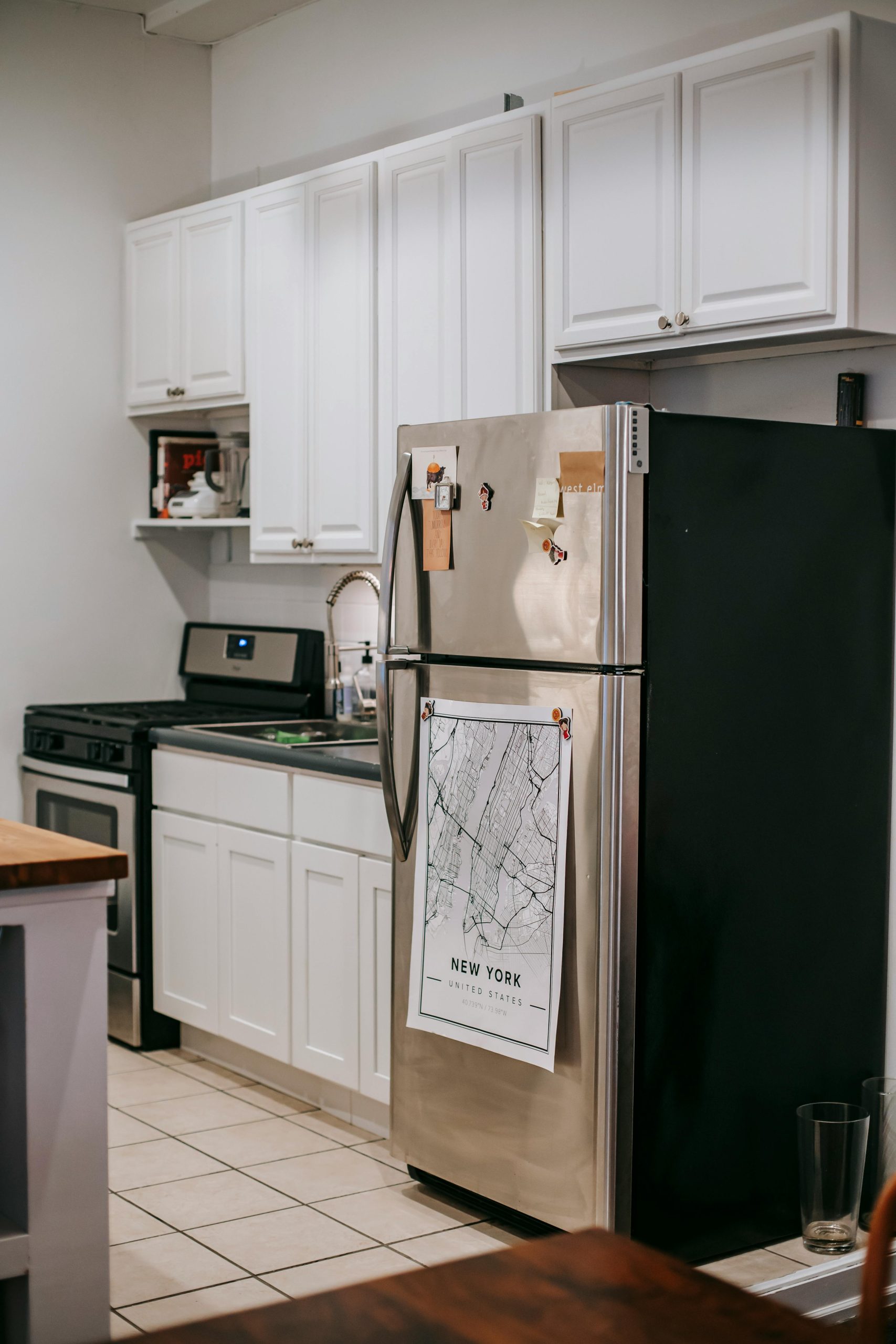 Modern light kitchen furnished with refrigerator and white cupboards placed near stove oven in modern cozy apartment with tiled floor